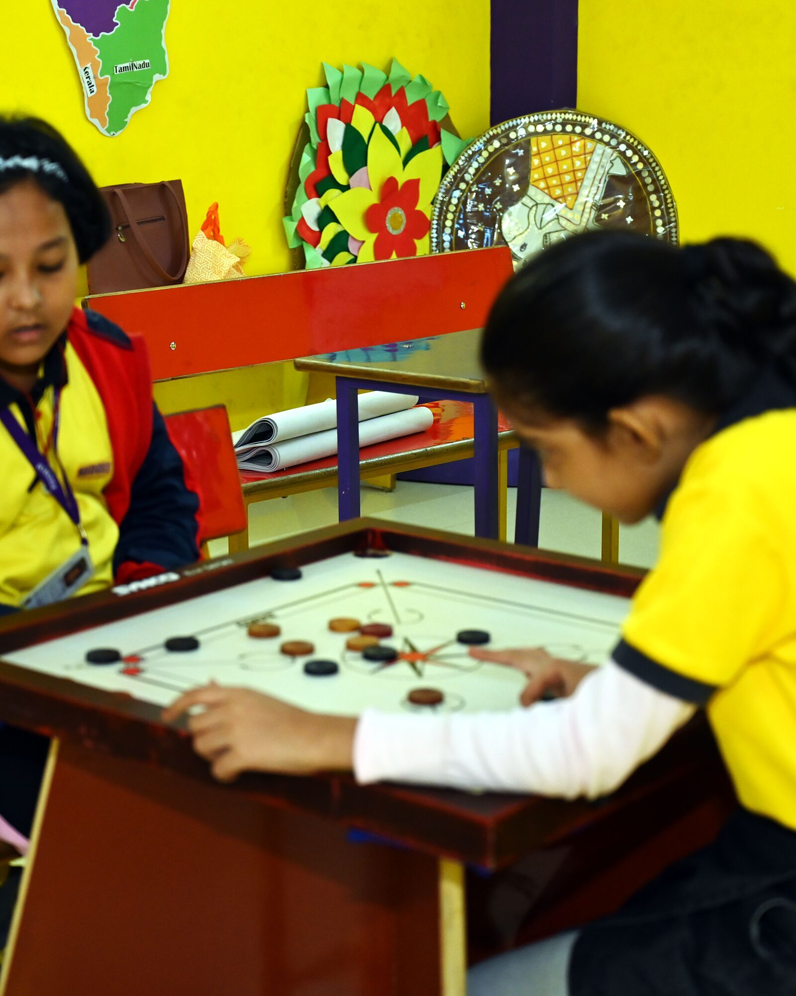 Two girls at a game of carrom in the games room, one lining up her shot