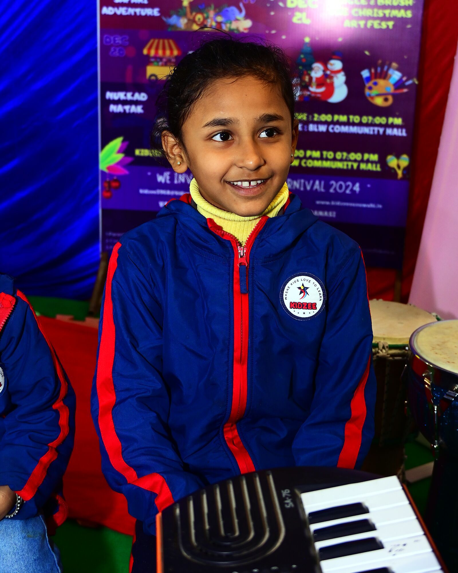 A girl smiling at the keyboard, drums beside her