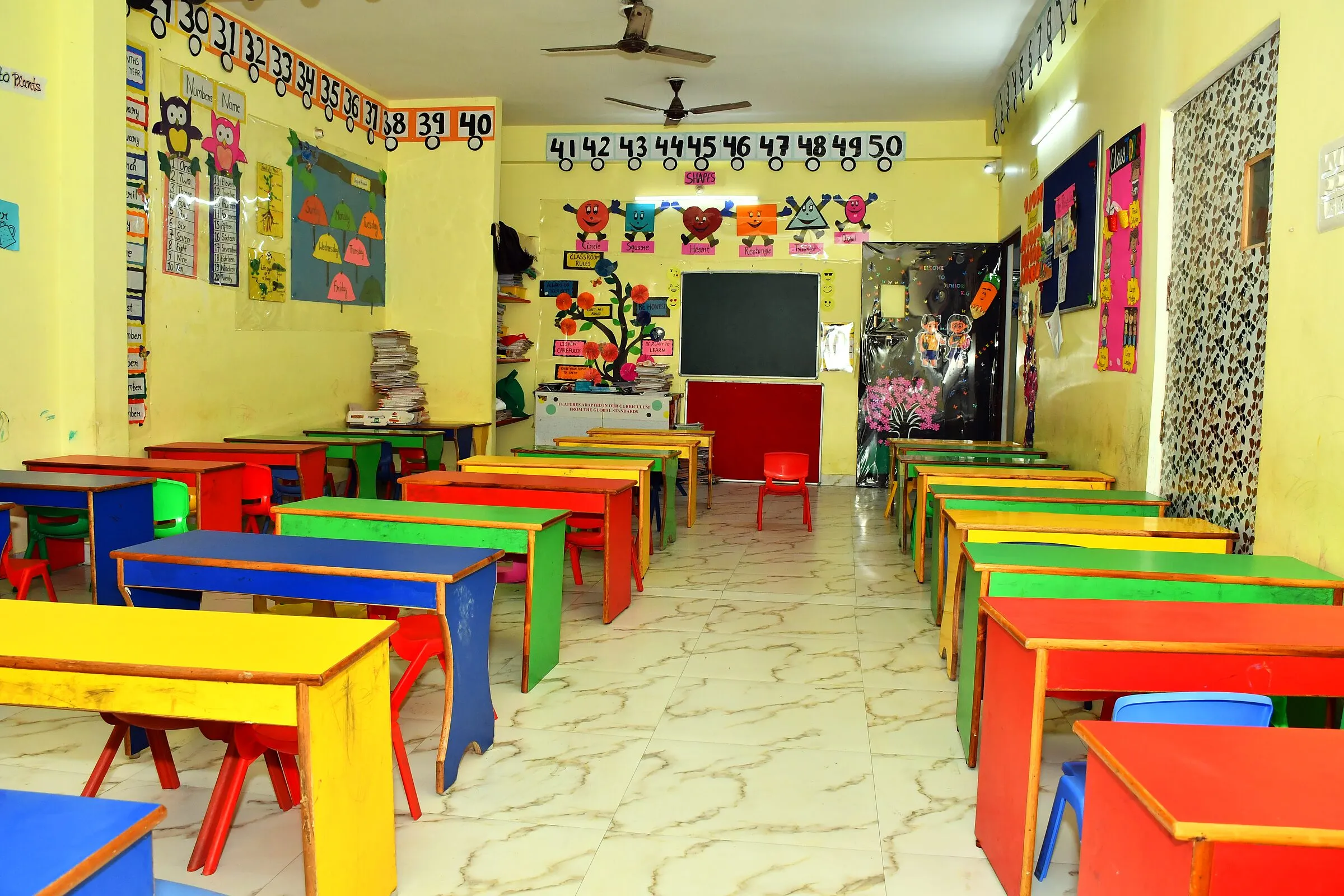 A classroom from the back: rows of coloured desks facing the blackboard