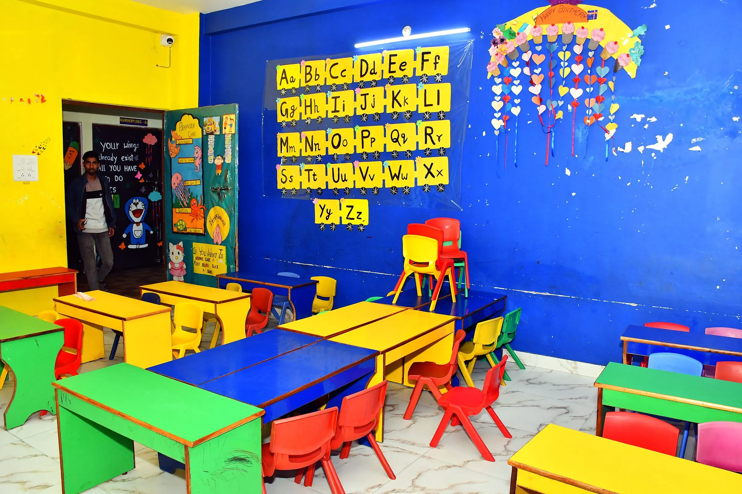 Desks before a blue wall with the alphabet on yellow cards
