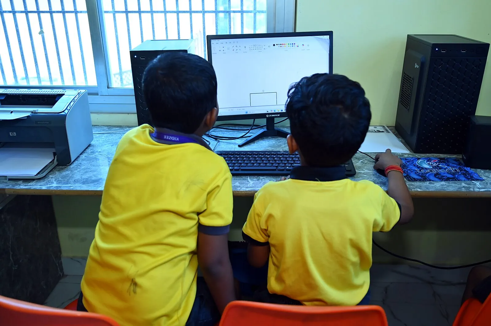 Two boys from behind at a computer in the lab, a printer beside them