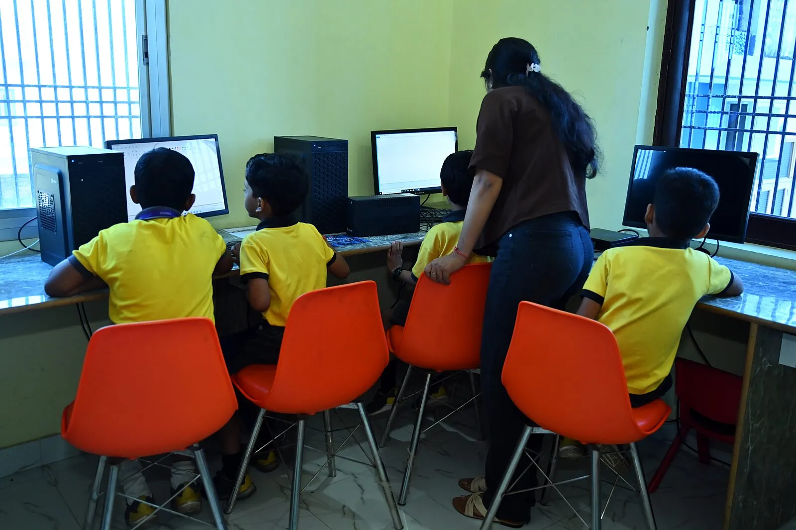Children at the lab's computers from behind, a teacher between them