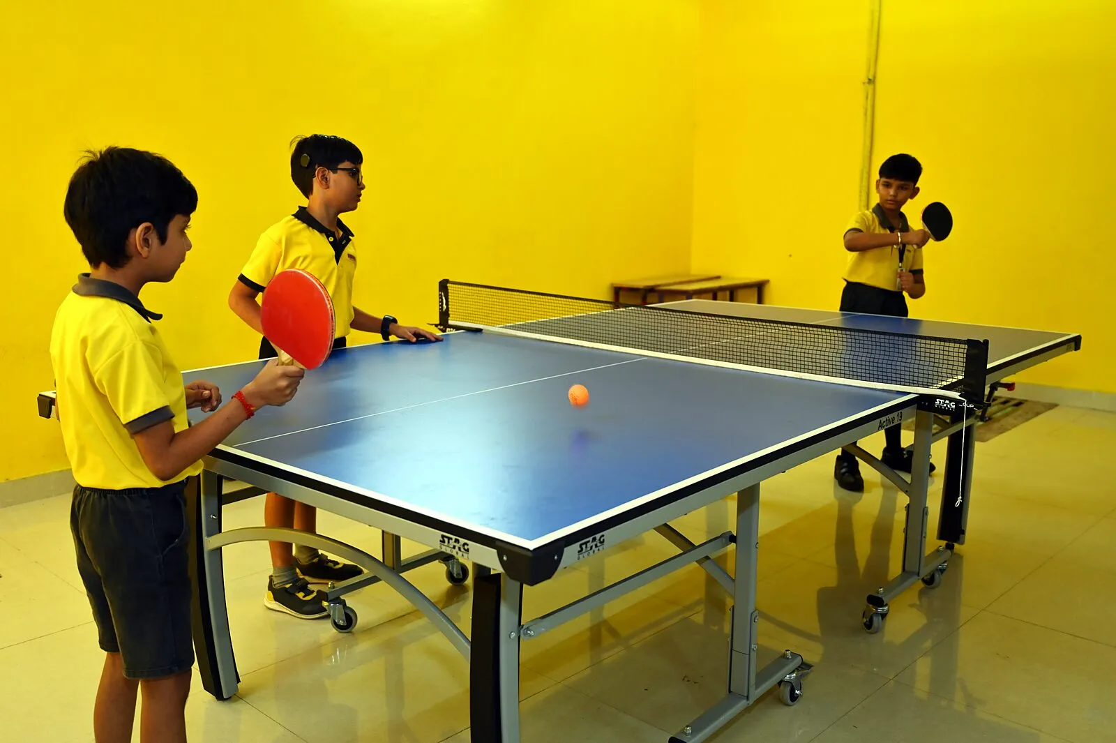 Two boys at the table tennis table, another waiting with his bat