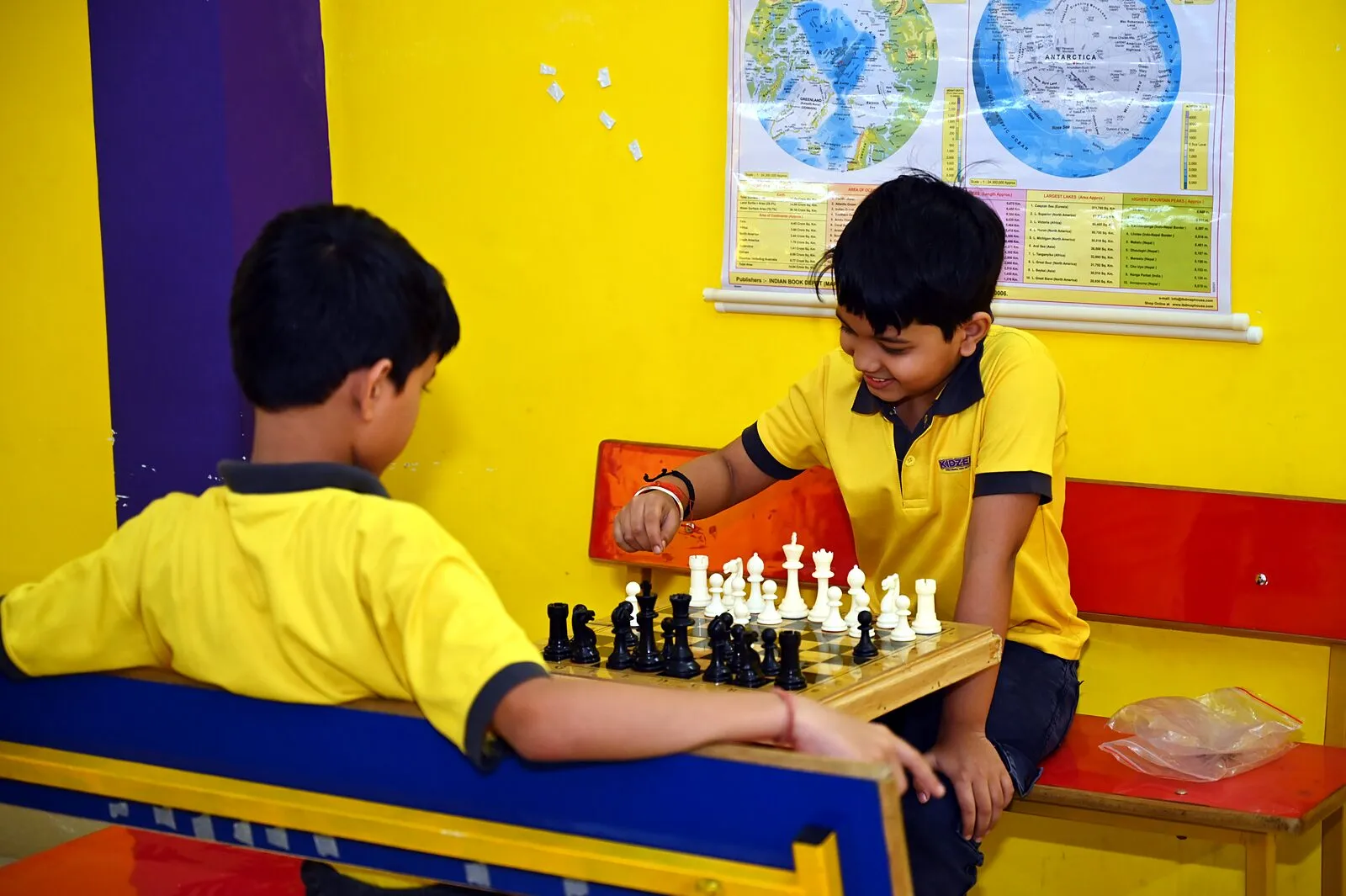 Two boys at chess on a bench by the wall map