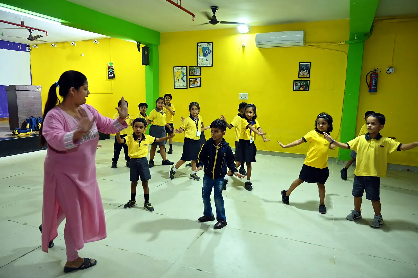 The hall, wide: a class spread across its floor for dance, their teacher leading at the side