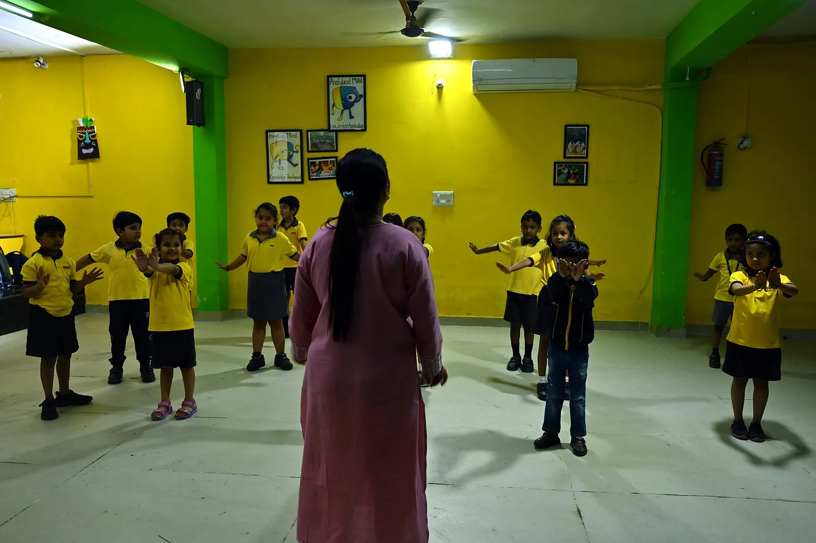 Down the hall from behind the teacher, the class copying the teacher's arms