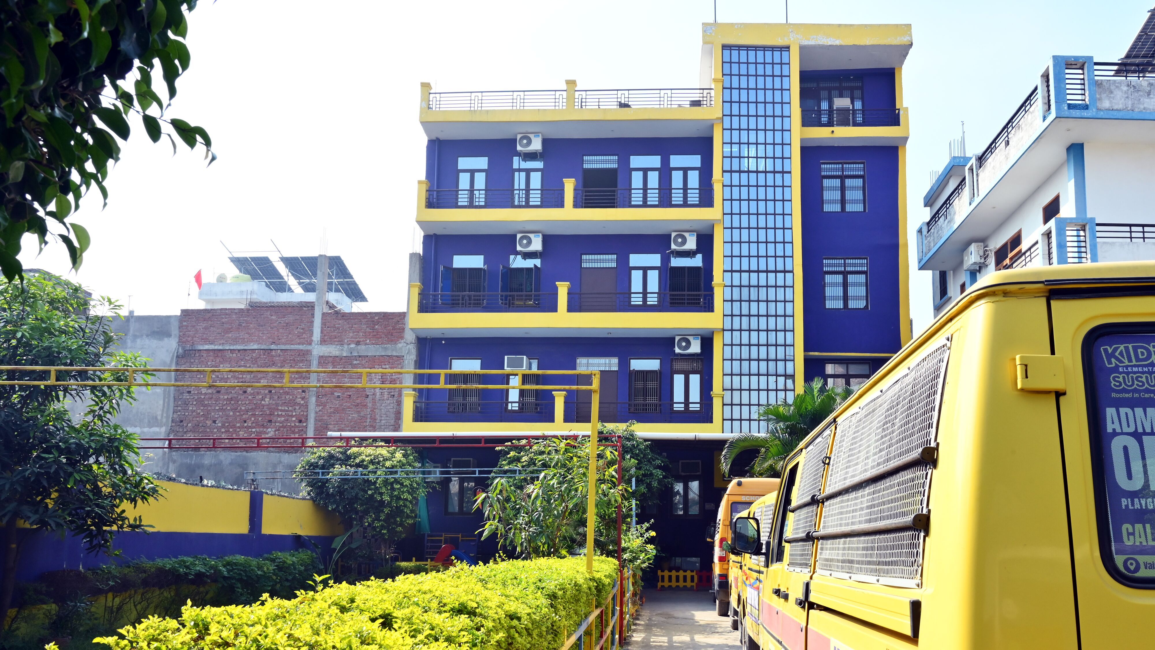 The path to the school's door between a trimmed hedge and the school vans, the purple and yellow building ahead