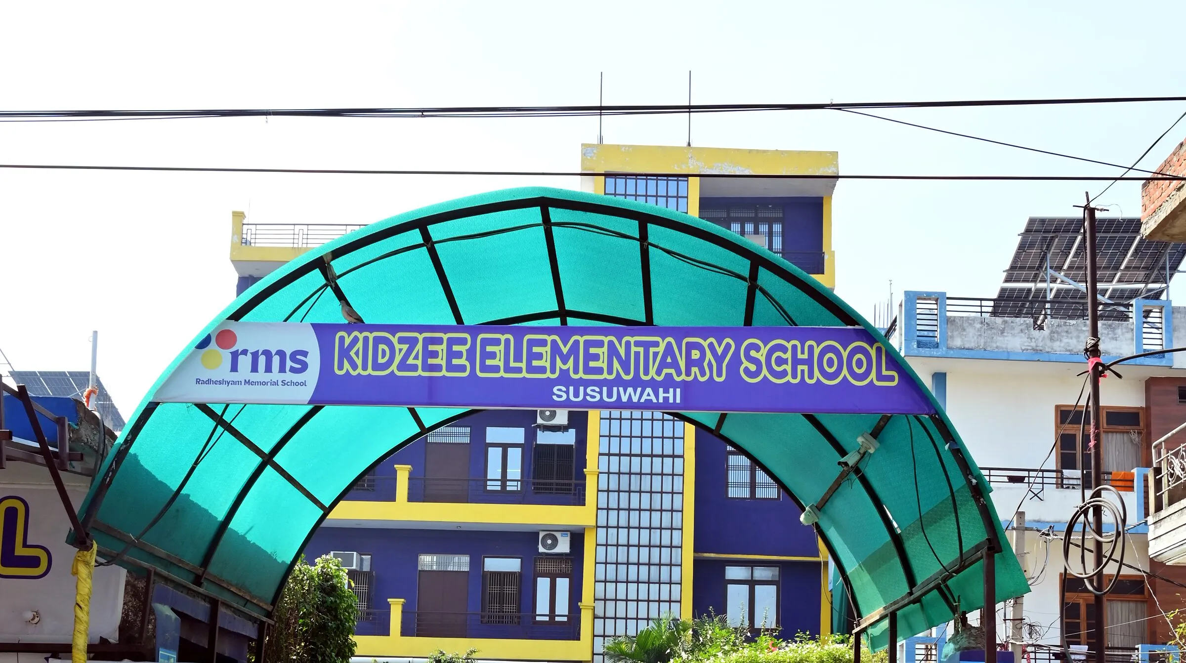 The gate from the road: its green arch with the rms mark and Kidzee Elementary School Susuwahi, the building behind