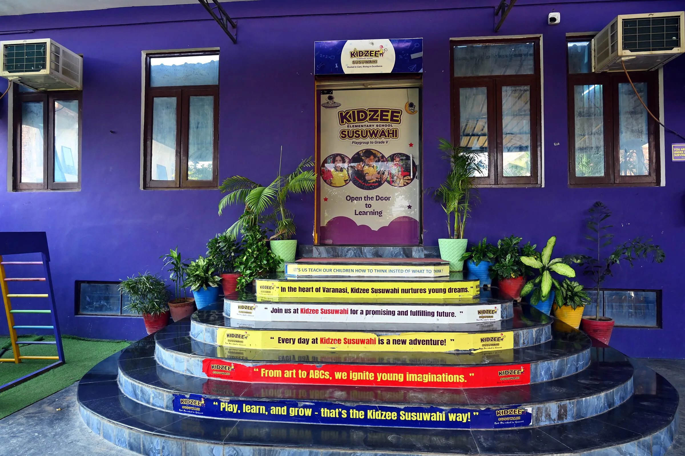 The front door at the top of the round steps, each step painted with a line of the school's, plants on either side