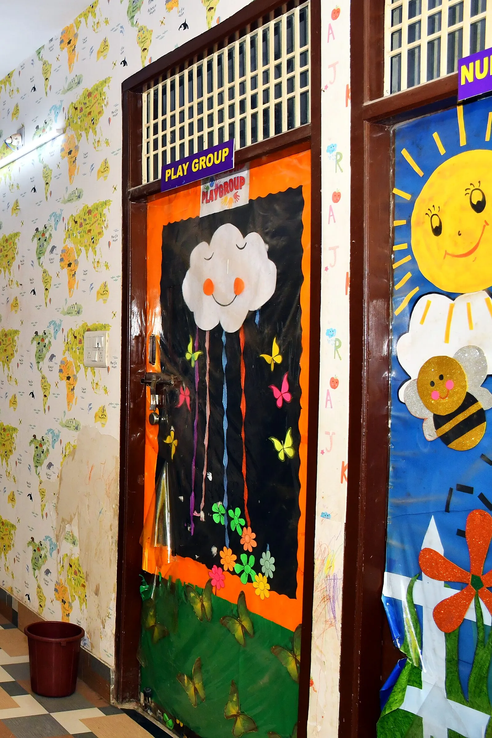 The Play Group's classroom door, decorated with a cloud and paper butterflies, beside the Nursery's smiling sun