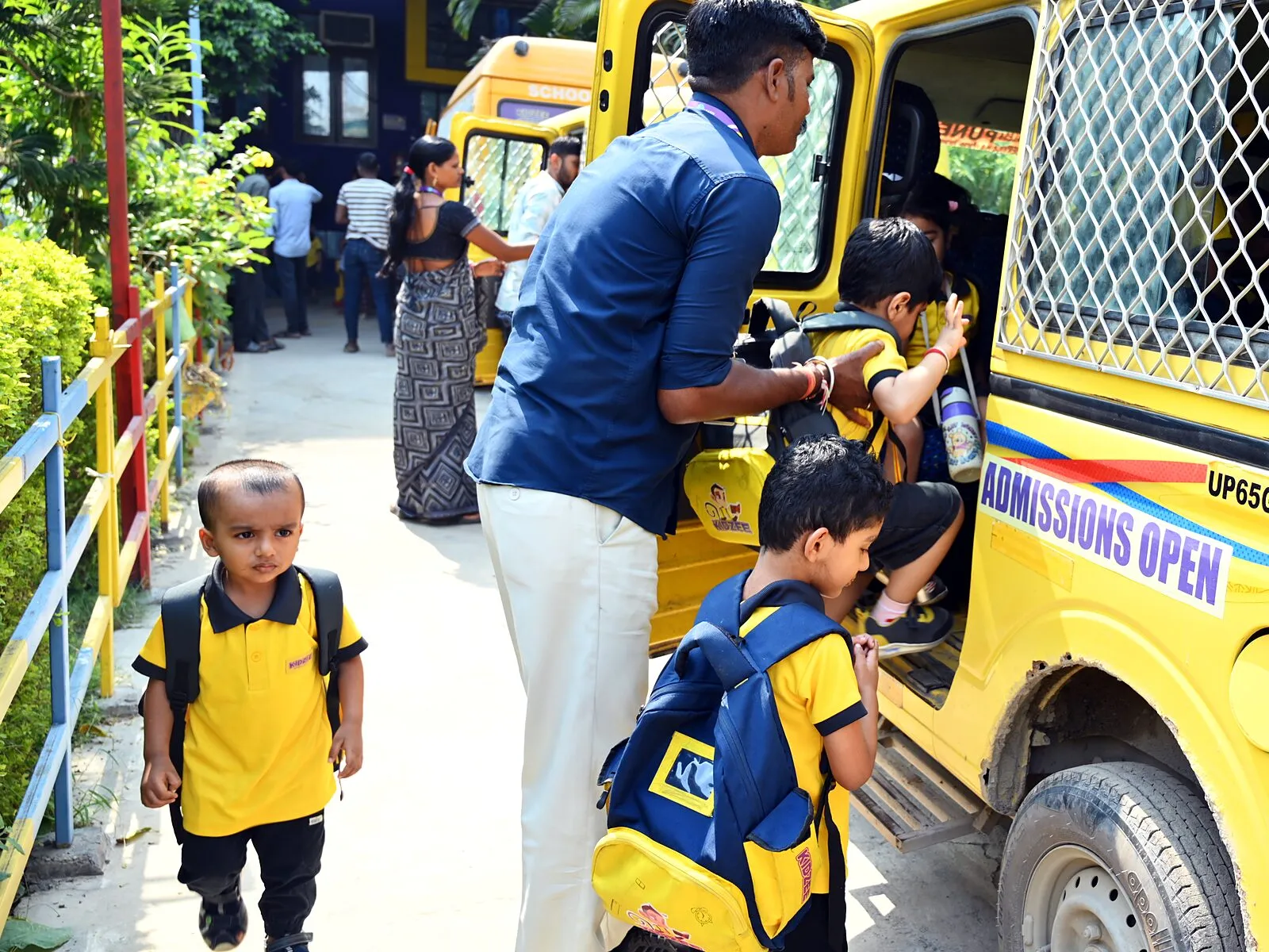A member of staff helping a small child up into one of the school vans, another child with a bag waiting