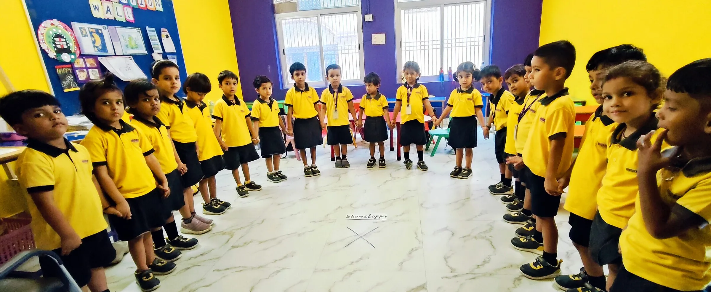 Children in uniform standing in a big circle on the classroom floor