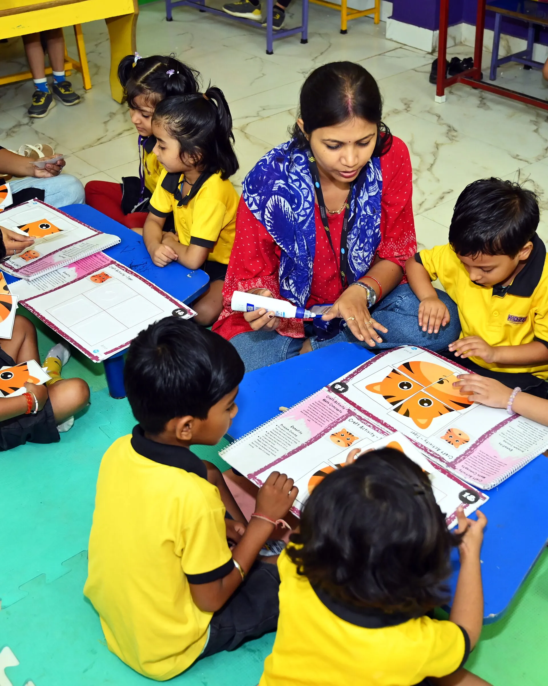 A teacher on the floor mats with children round a low table, each with a big book open at a paper tiger
