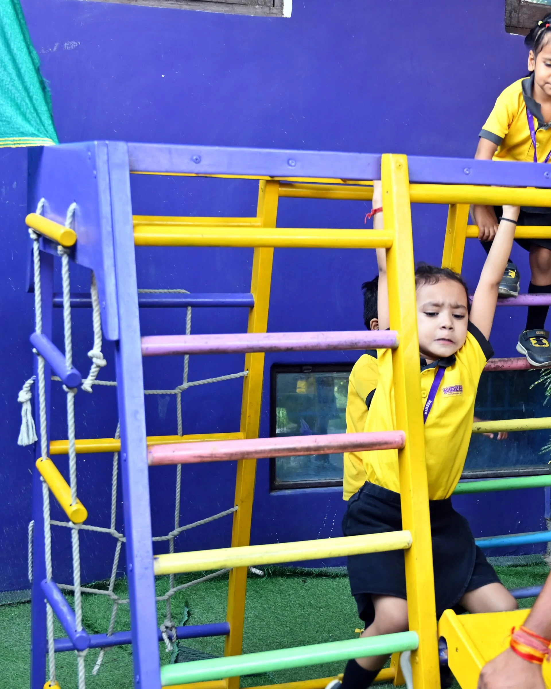 A boy hanging from the bars of the climbing frame, a girl at the top