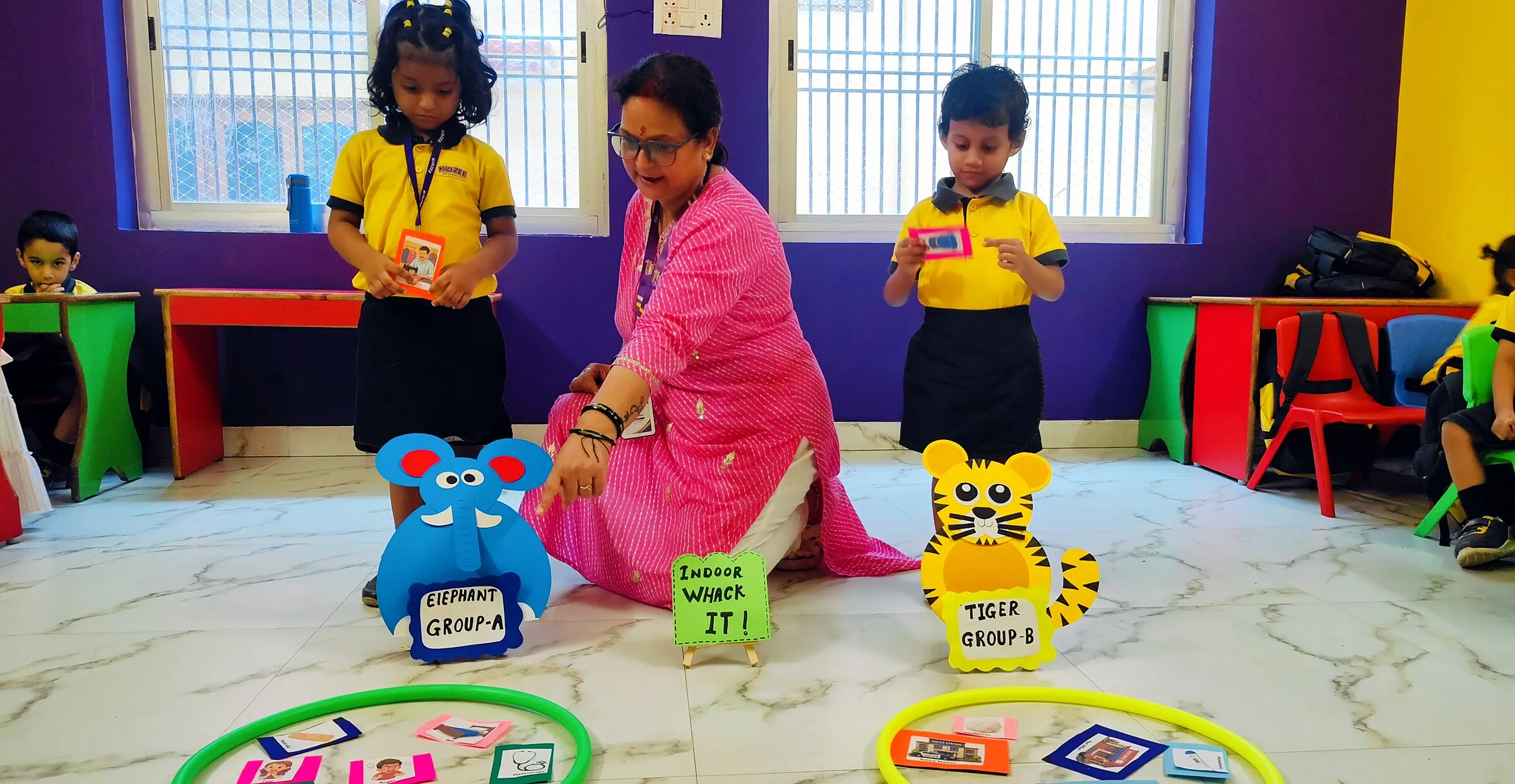 A teacher kneeling with children on the classroom floor for a game with hoops and picture cards