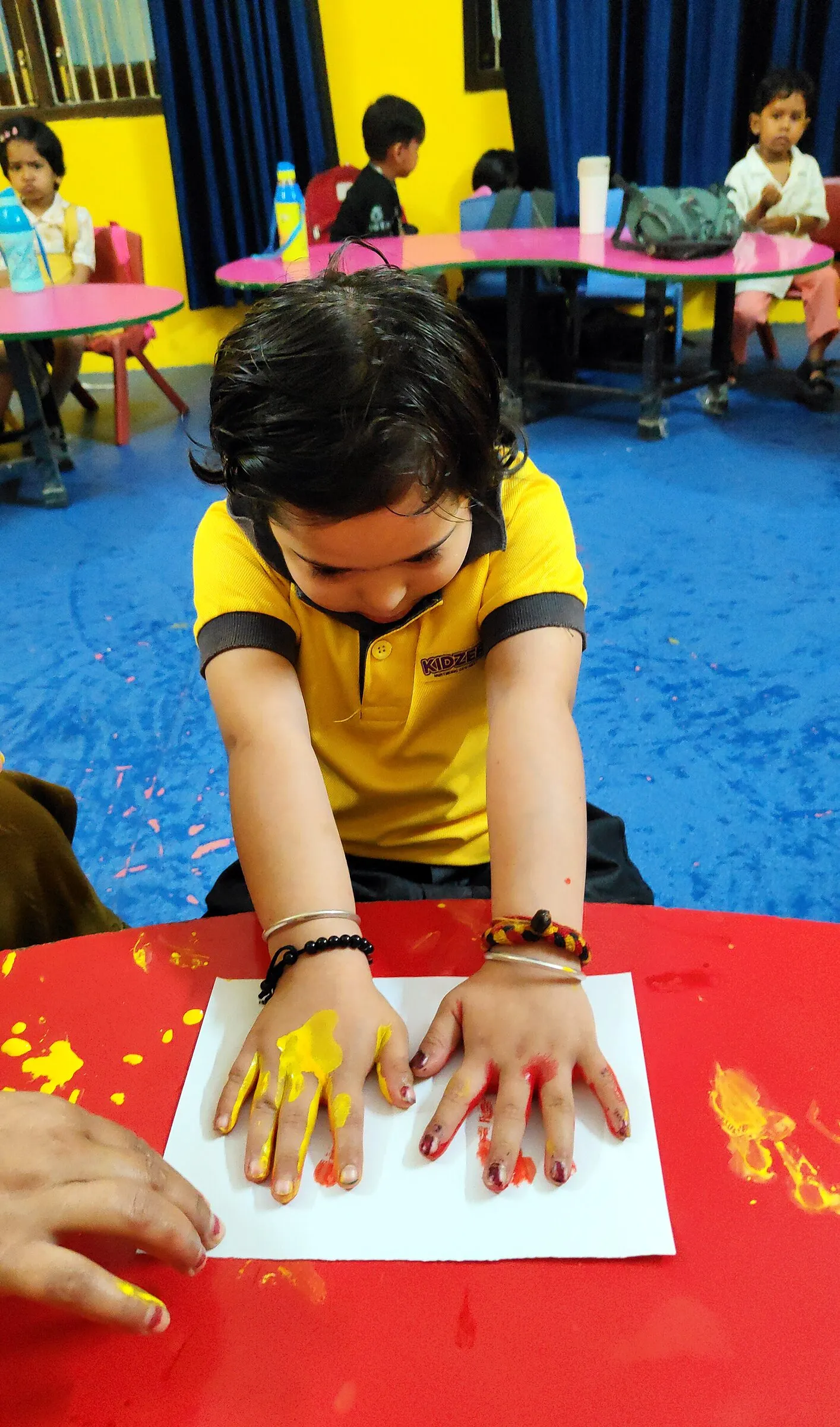 A girl pressing her yellow-painted hands onto paper
