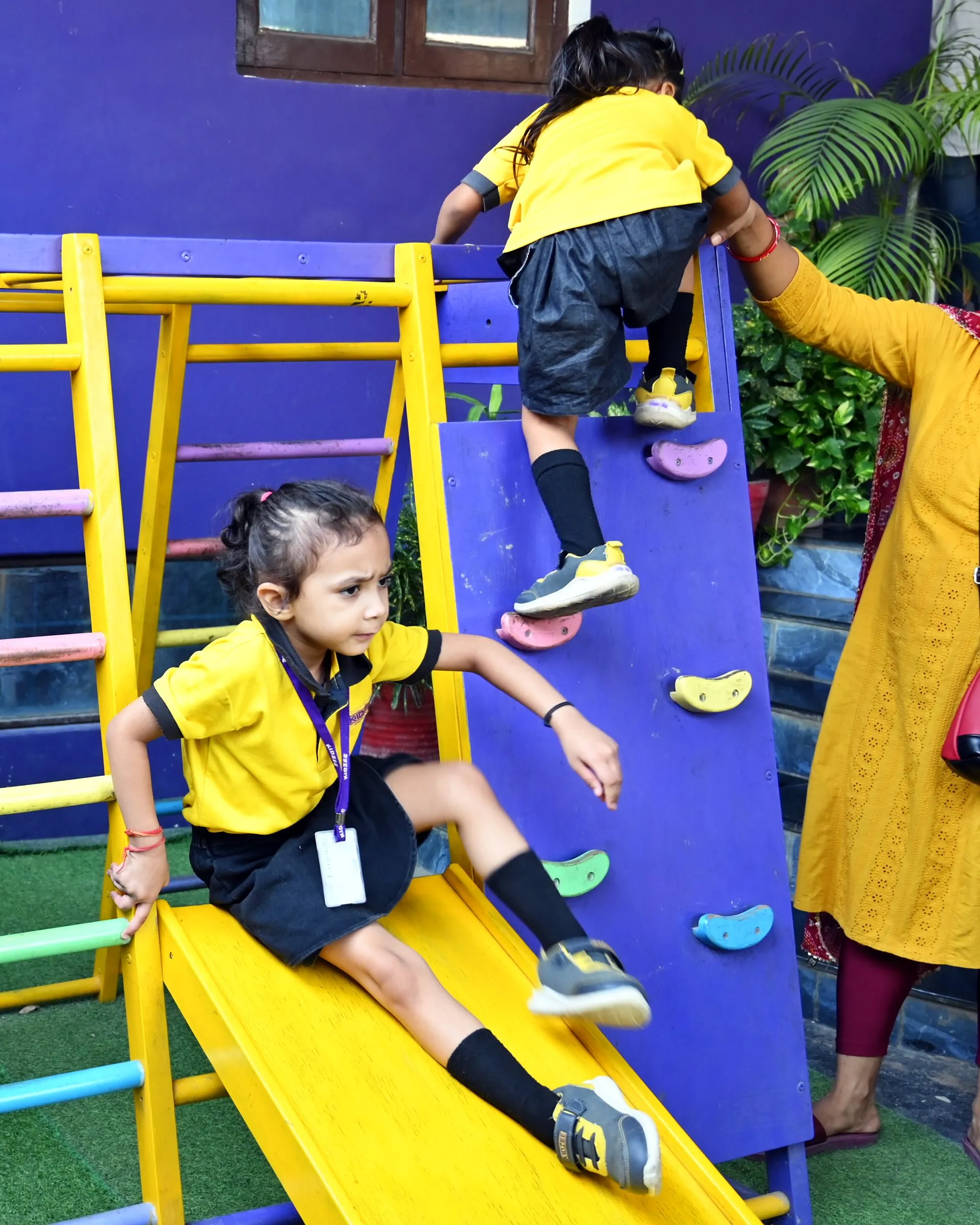 A girl coming down the slide, a grown-up's hand holding the girl climbing the wall above her