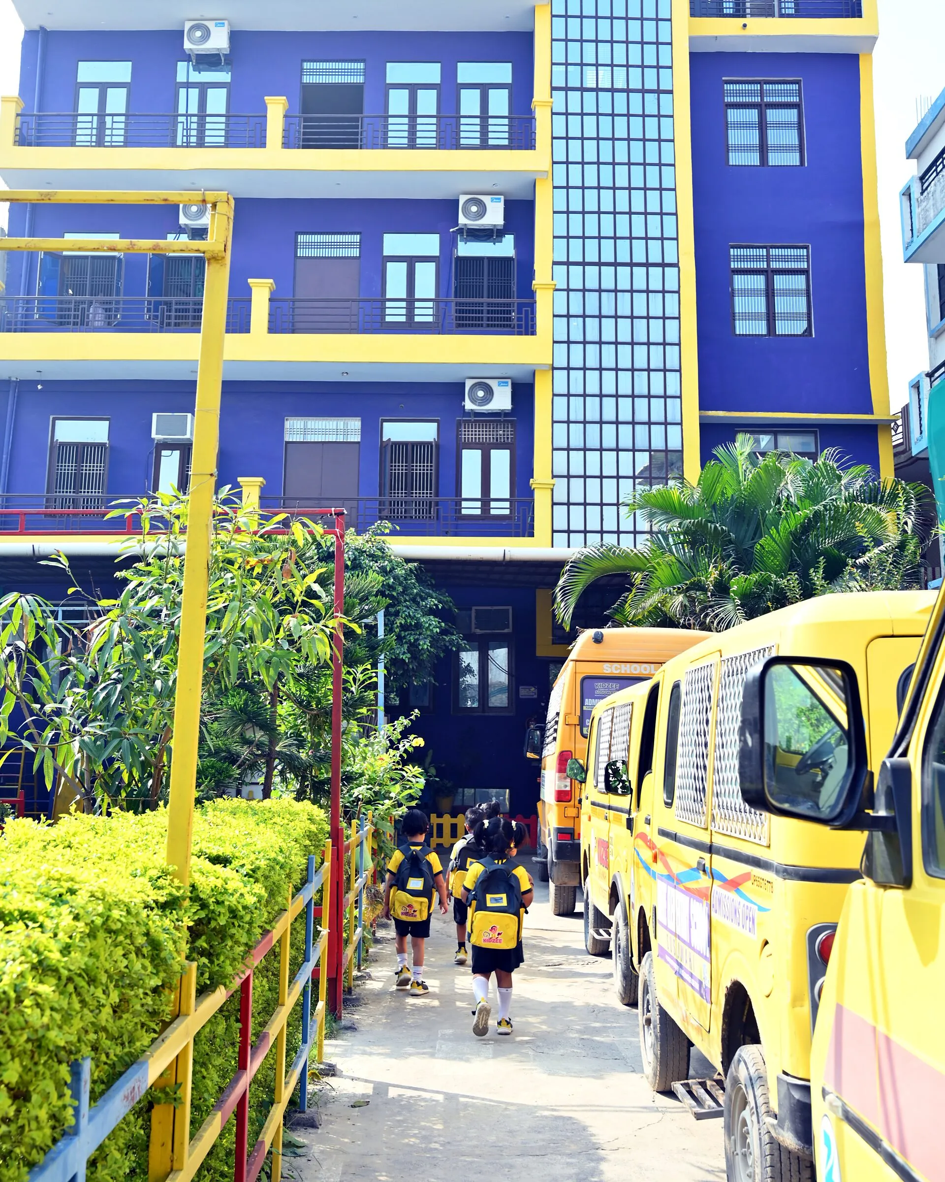 Children with school bags walking up the path to the school's door, seen from behind, the vans parked beside them