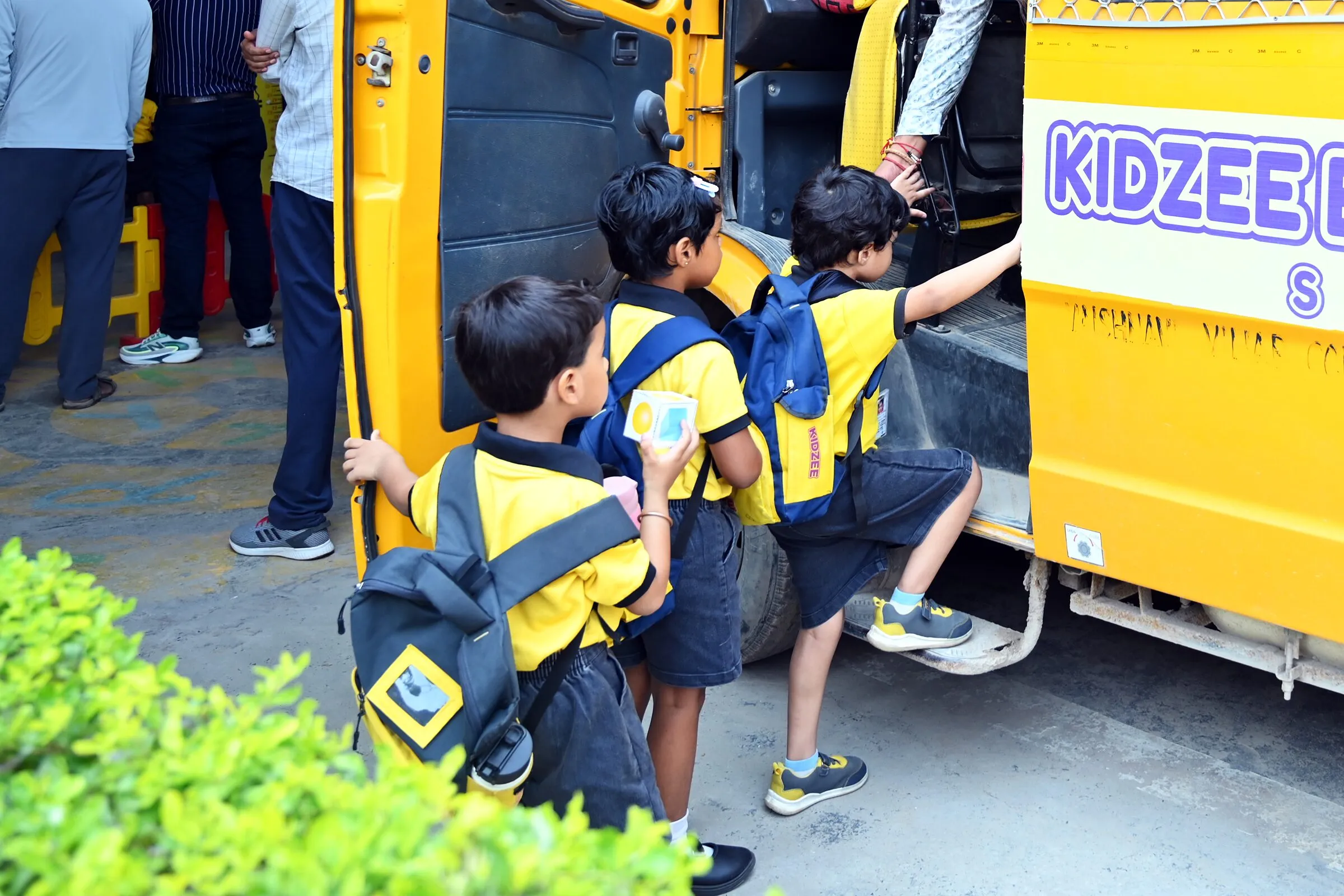 Three children with school bags climbing into a school van, seen from behind, a hand reaching to help them in