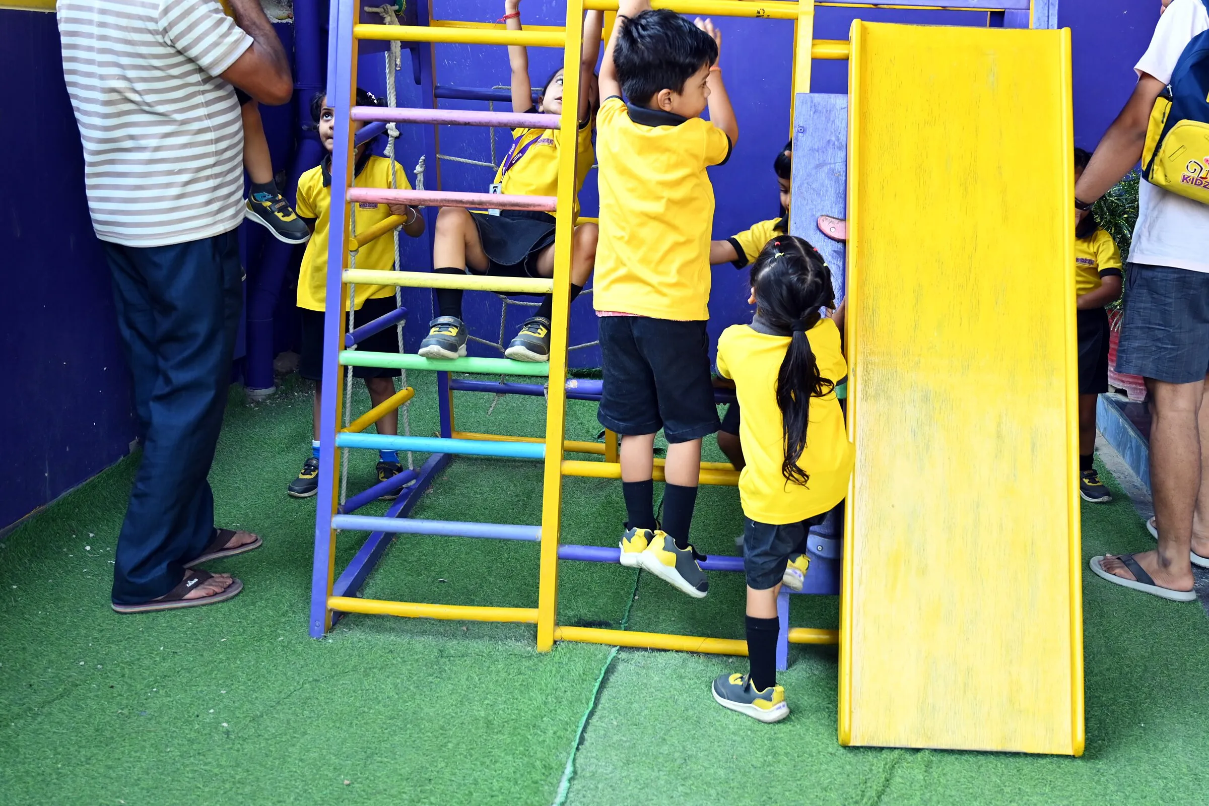 Small children climbing the frame beside the slide, their families standing by