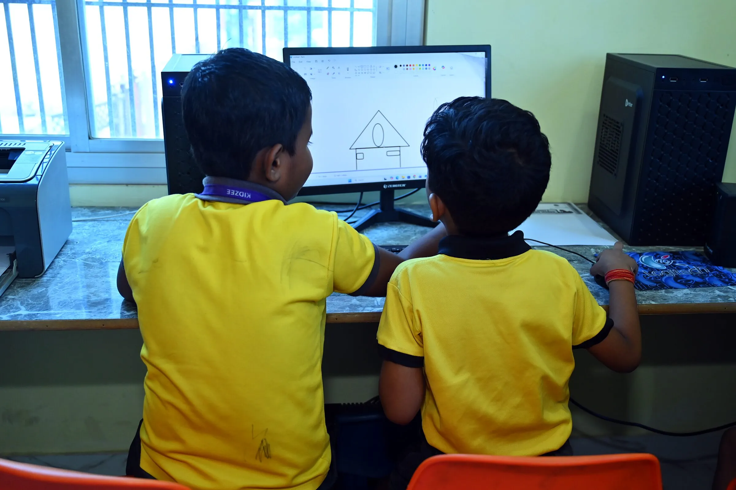 Two boys at a computer in the lab, seen from behind, a house they drew on the screen