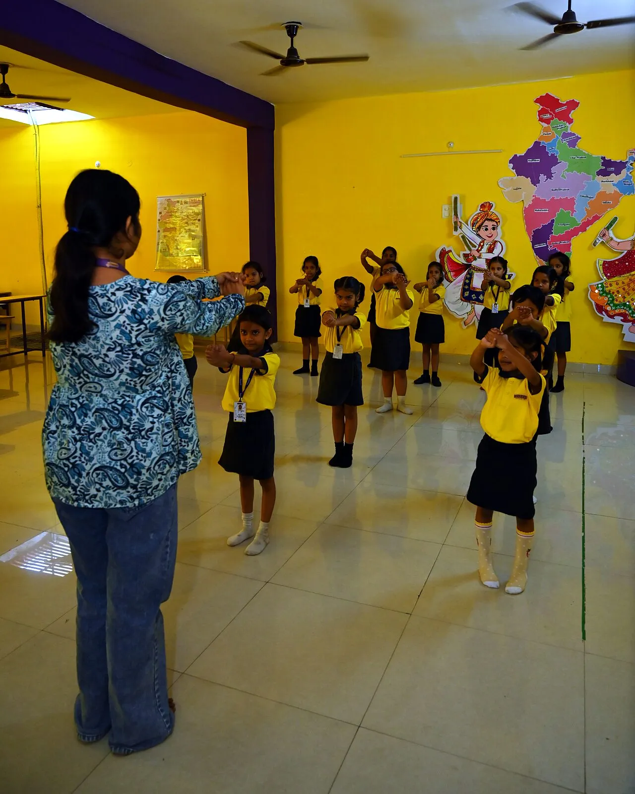 Children in the hall copying their teacher's arms, stretched out in front of them