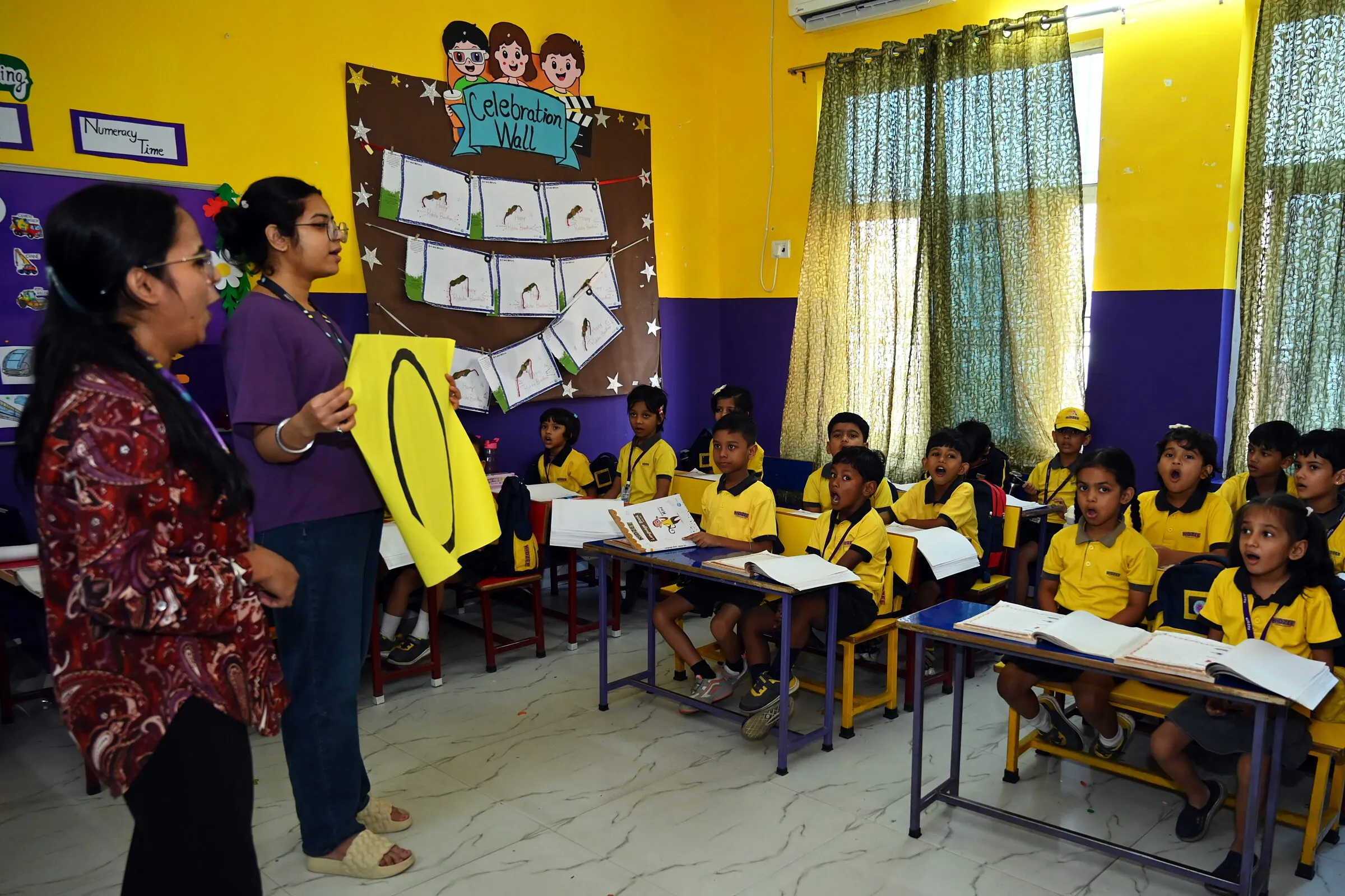 Two teachers at the front holding up a big zero, the class at its desks answering