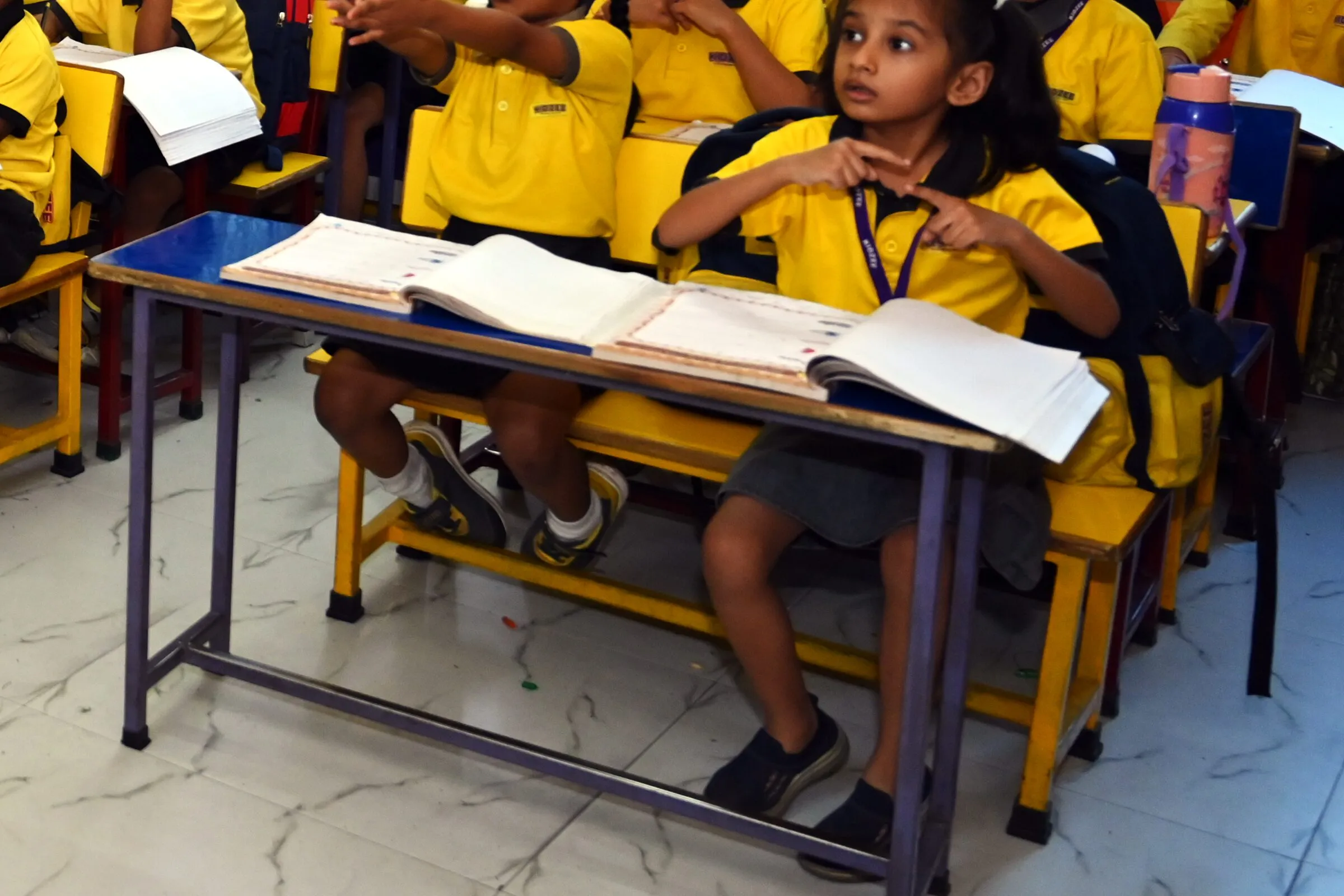 A girl at her desk listening to the teacher, her writing books open in front of her
