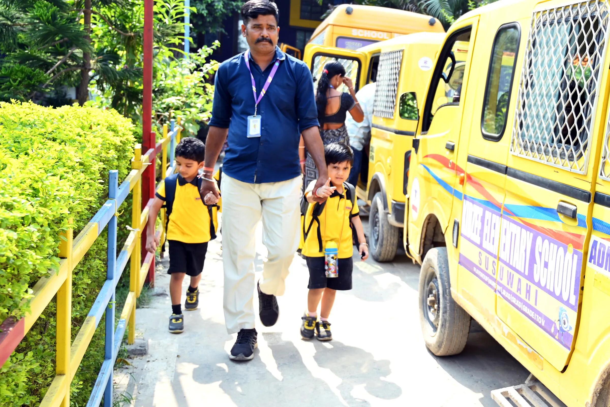 A member of staff walking two children along the path past the school vans