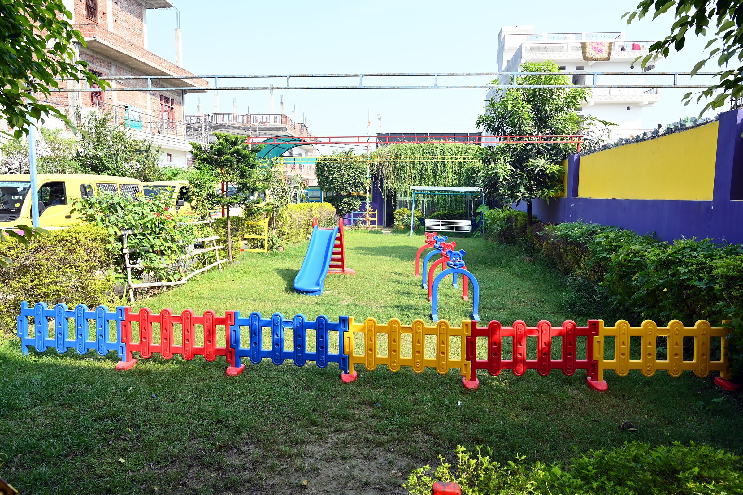 The playground across the lawn: a slide, rockers and a low fence in bright colours