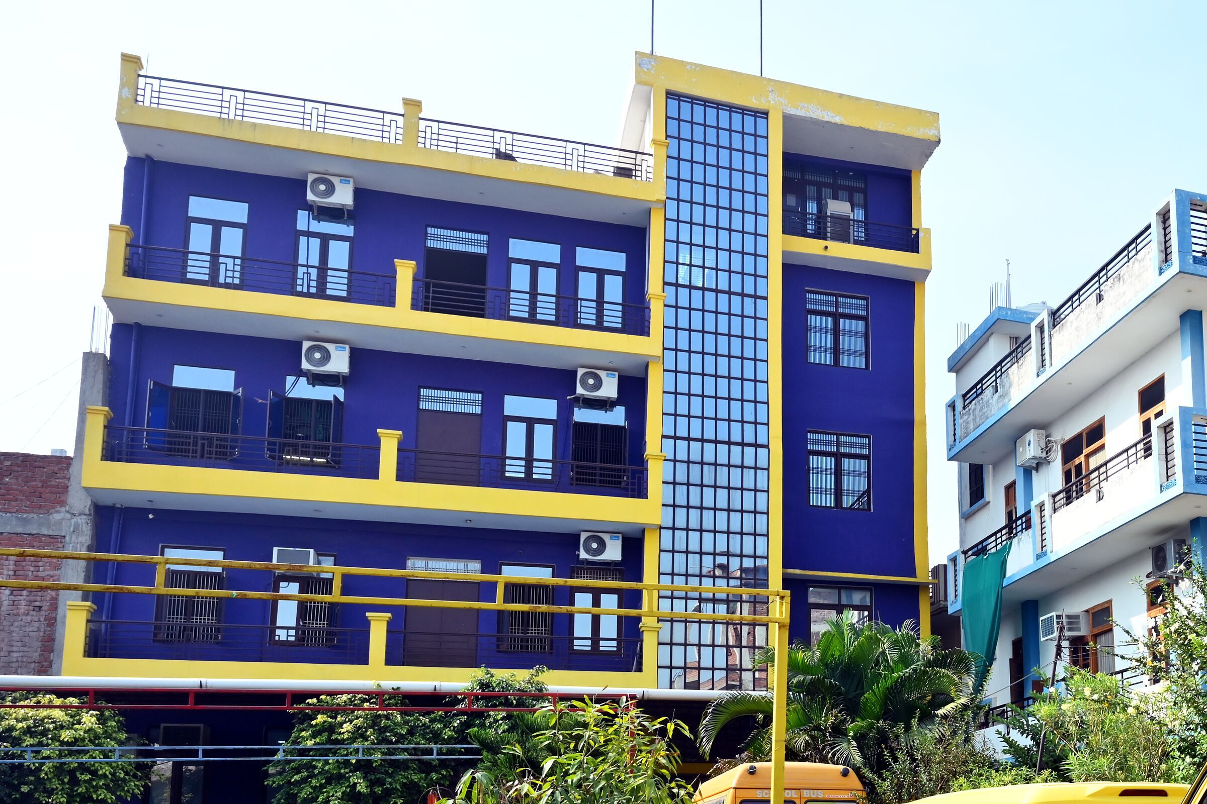 The purple and yellow school building across its lawn and hedge, the school vans along the drive