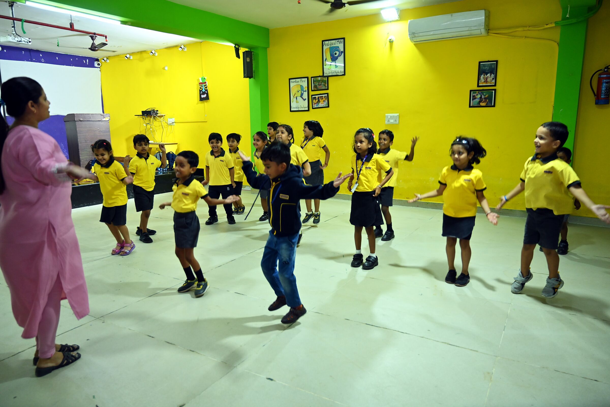 The hall, its floor filled by a class at dance, their teacher leading at the side