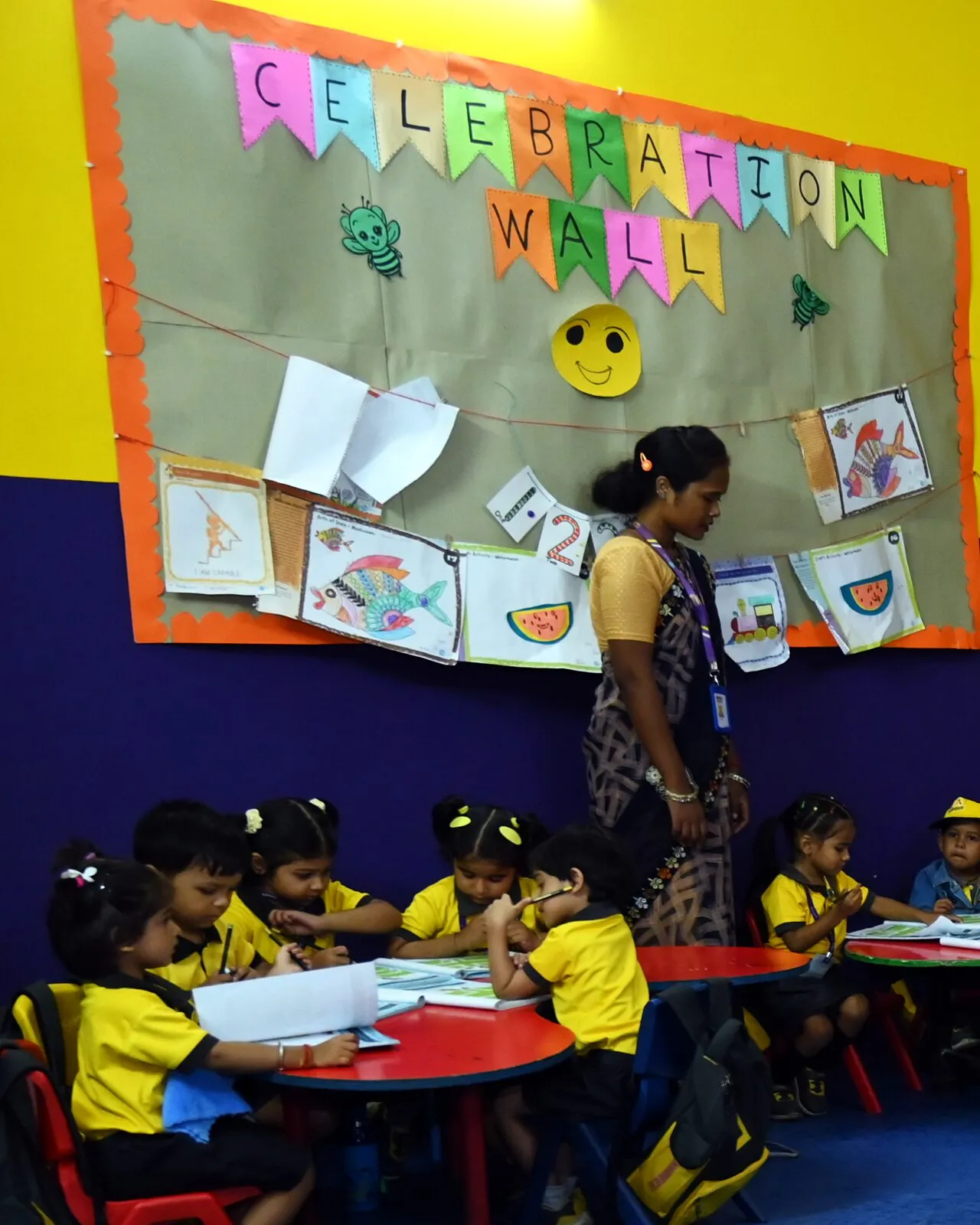 The class's coloured work on its Celebration Wall, fish and watermelons, the children at work below with their teacher