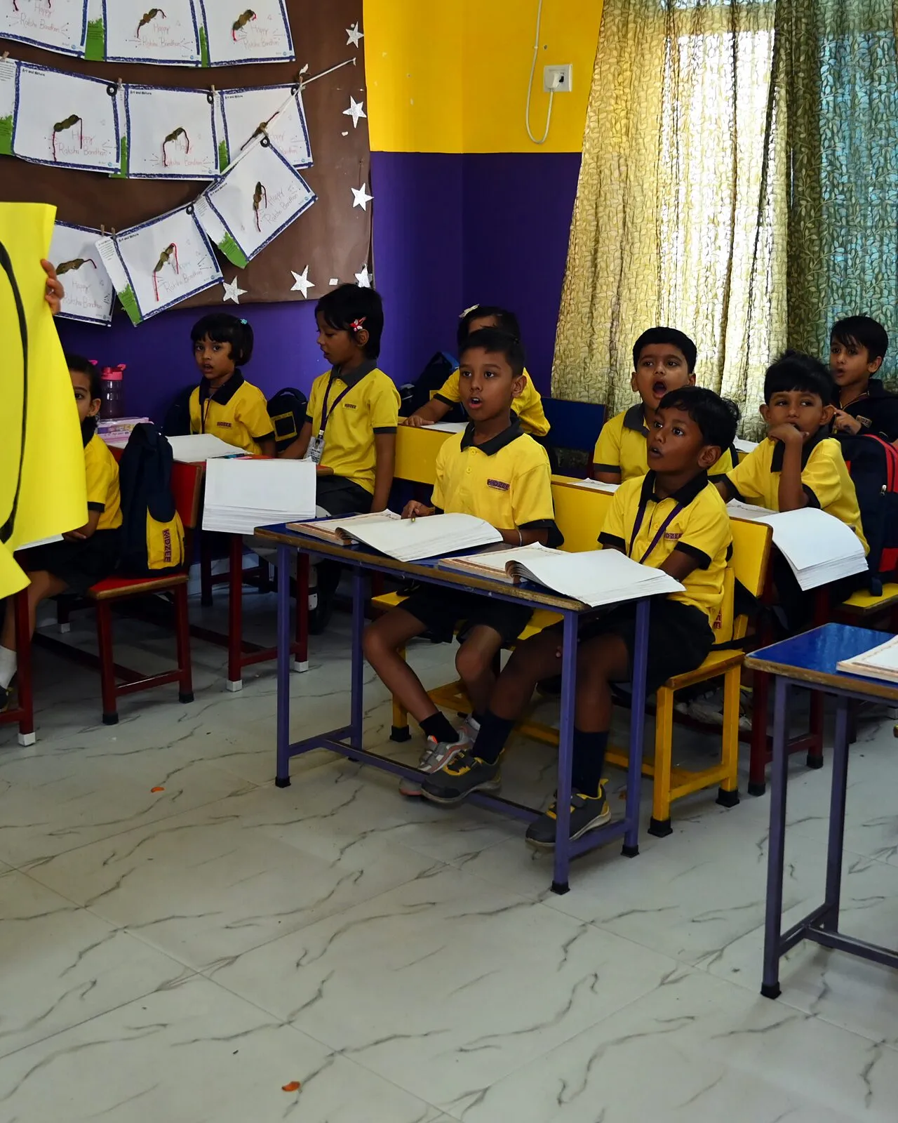Children at their desks with their books open, turned to the teacher