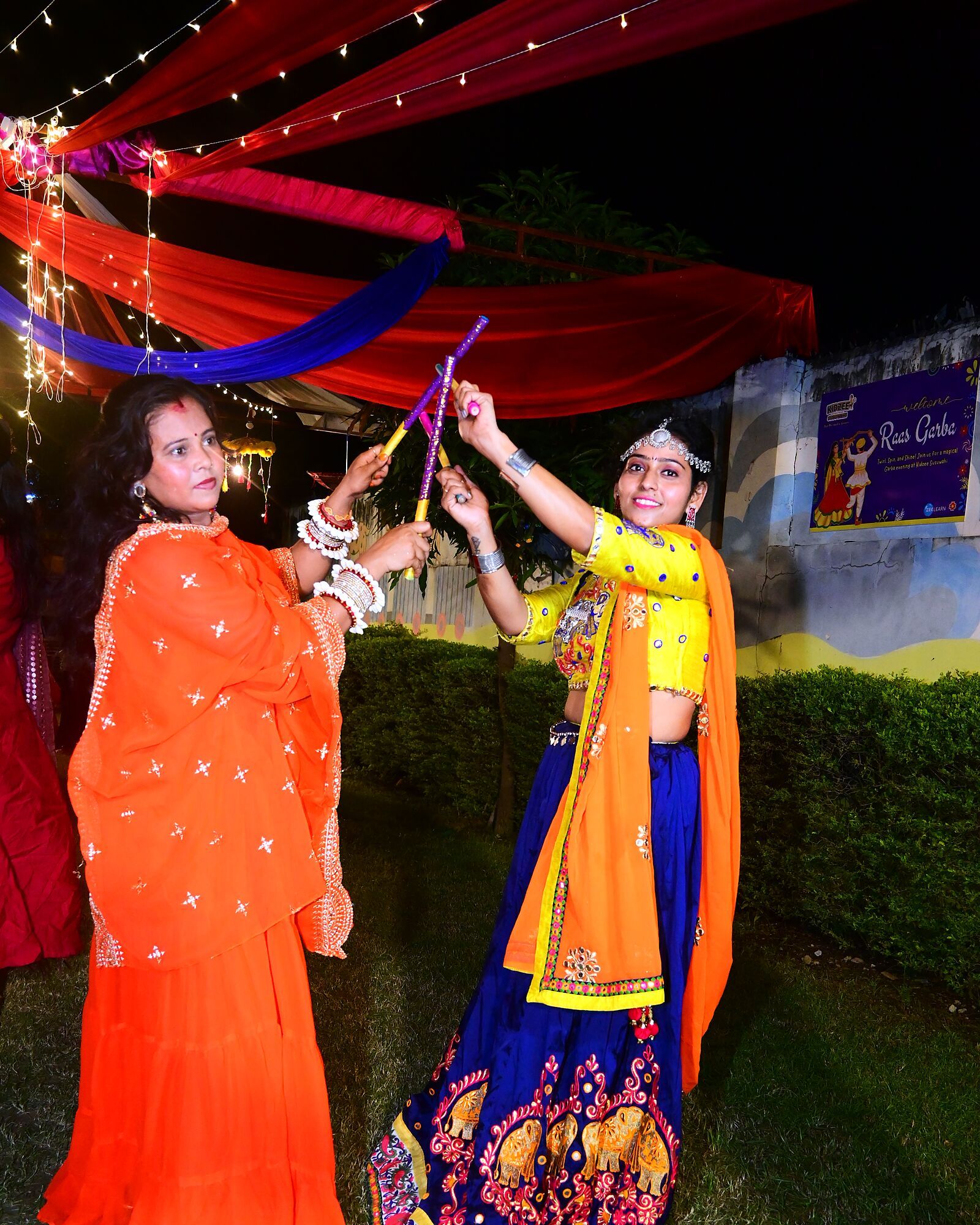 Two teachers dancing with dandiya sticks at night