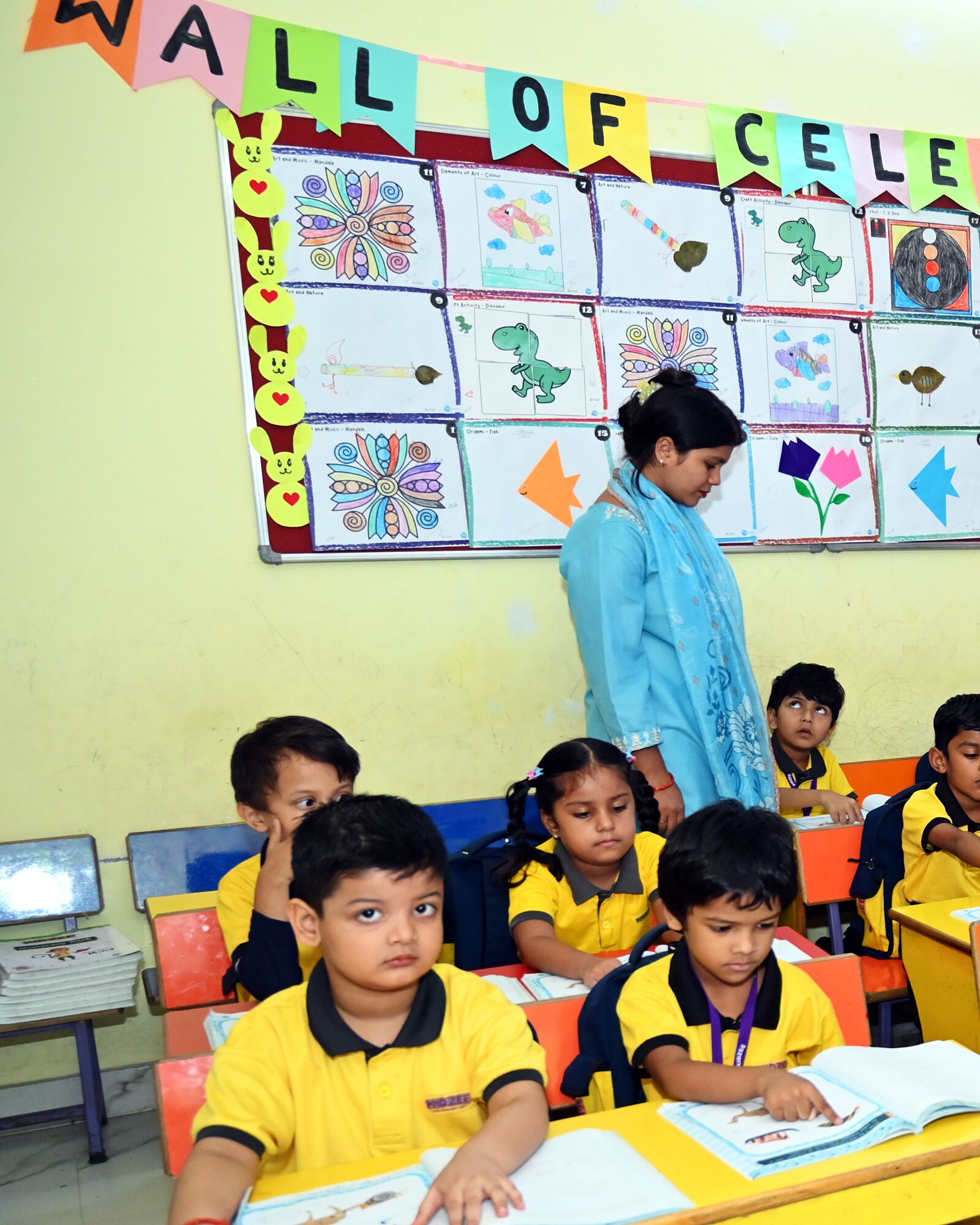 Children at their books under the Wall of Celebration, the class's own artwork, their teacher among them
